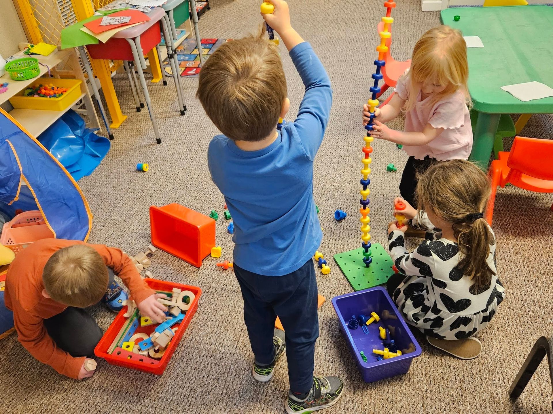 Children playing with colorful bead mazes and toys on a classroom carpet