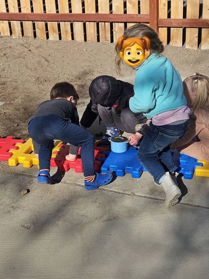 Three children playing with colorful interlocking blocks outdoors on a concrete surface