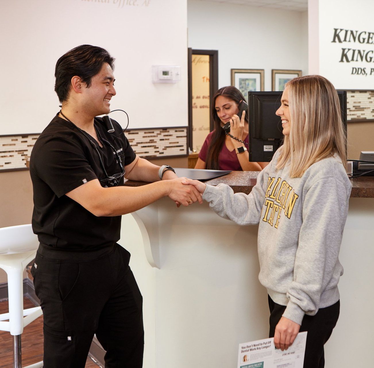 A man and woman shaking hands in front of a sign that says kings dental