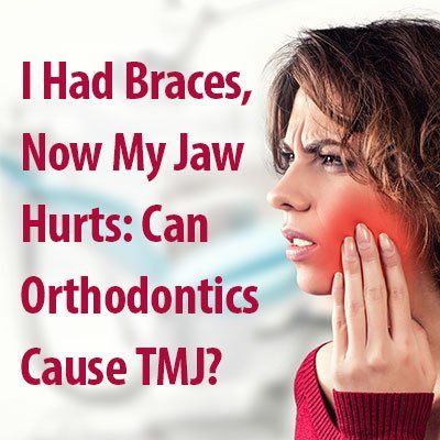 A woman with braces on her teeth is holding her jaw in pain