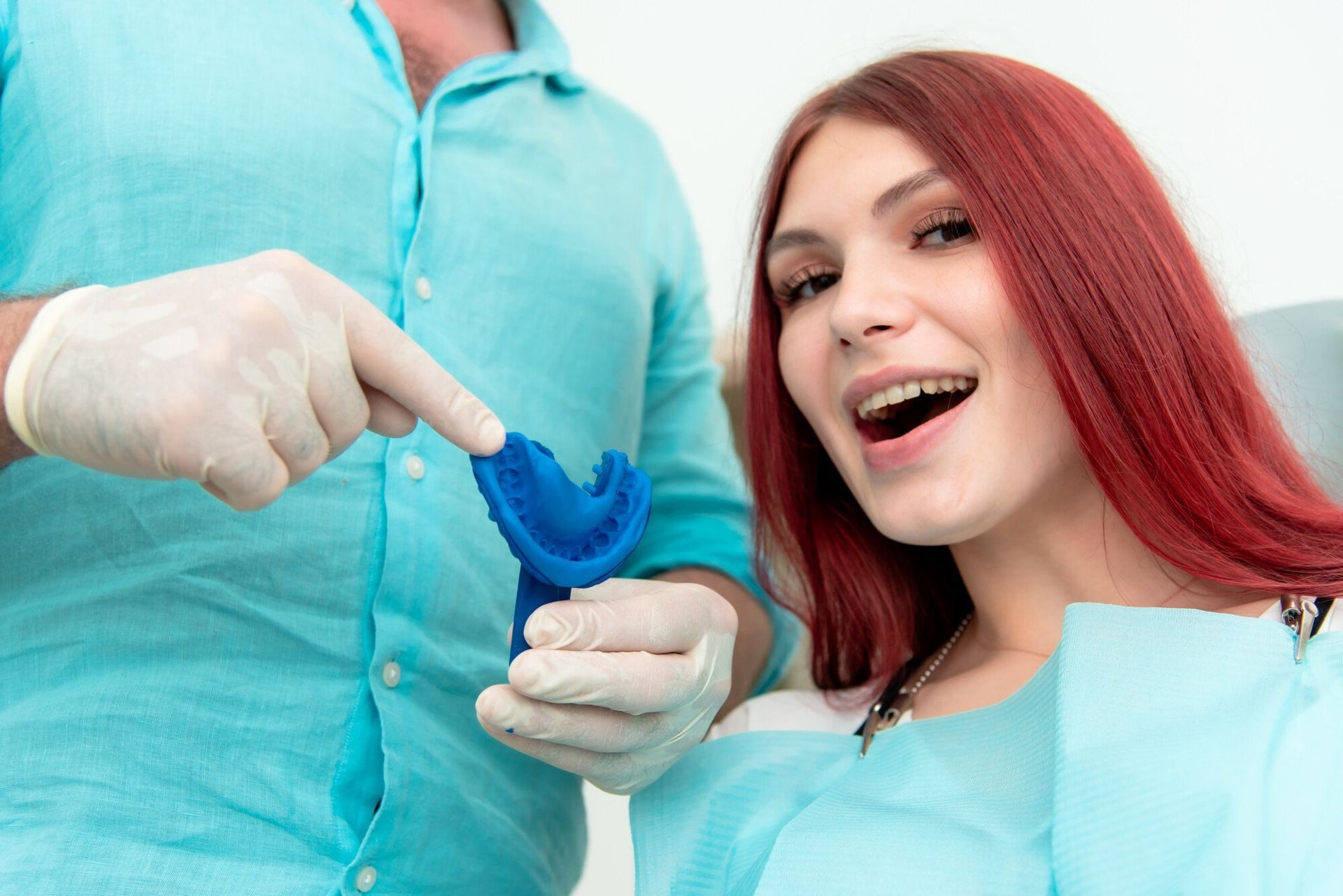 A woman is sitting in a dental chair while a dentist holds a blue mouth guard.