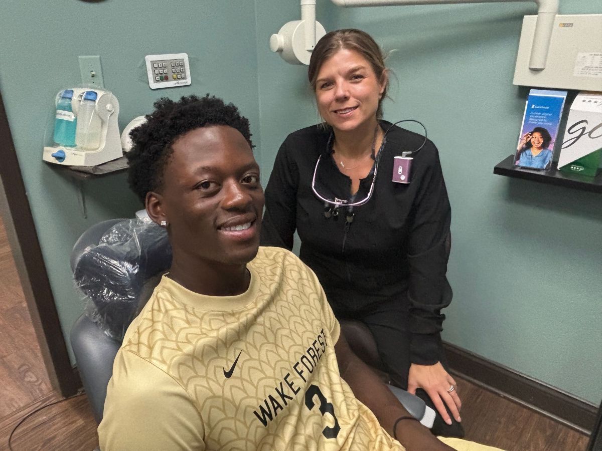 A man in a wake forest shirt is sitting in a dental chair next to a woman.