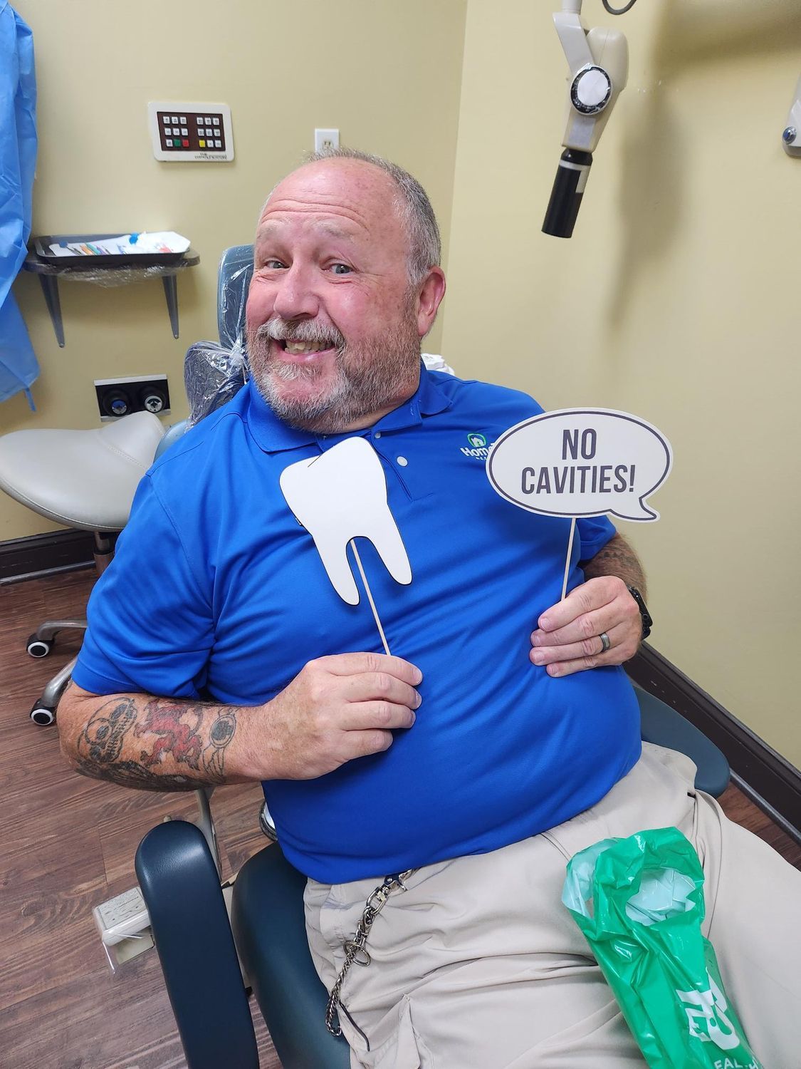 Hombre con camisa azul en el dentista, sosteniendo un diente y un cartel que dice 