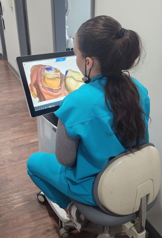 Una mujer con uniforme médico mira un modelo dental digital en una pantalla en un pasillo.