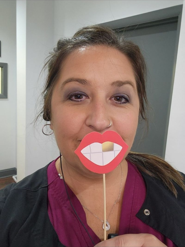 Mujer sosteniendo un recorte de papel de dientes, uno de ellos de color dorado, sonriendo frente a su boca.