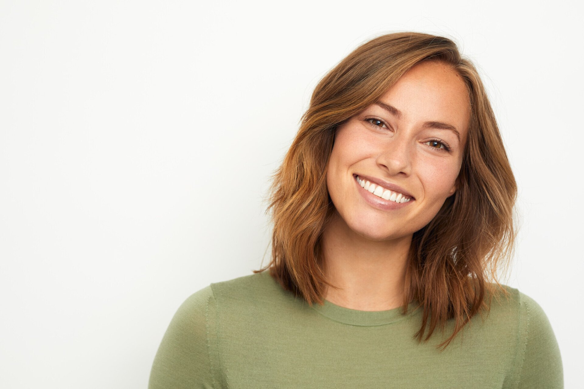 A woman in a green sweater is smiling and looking at the camera.