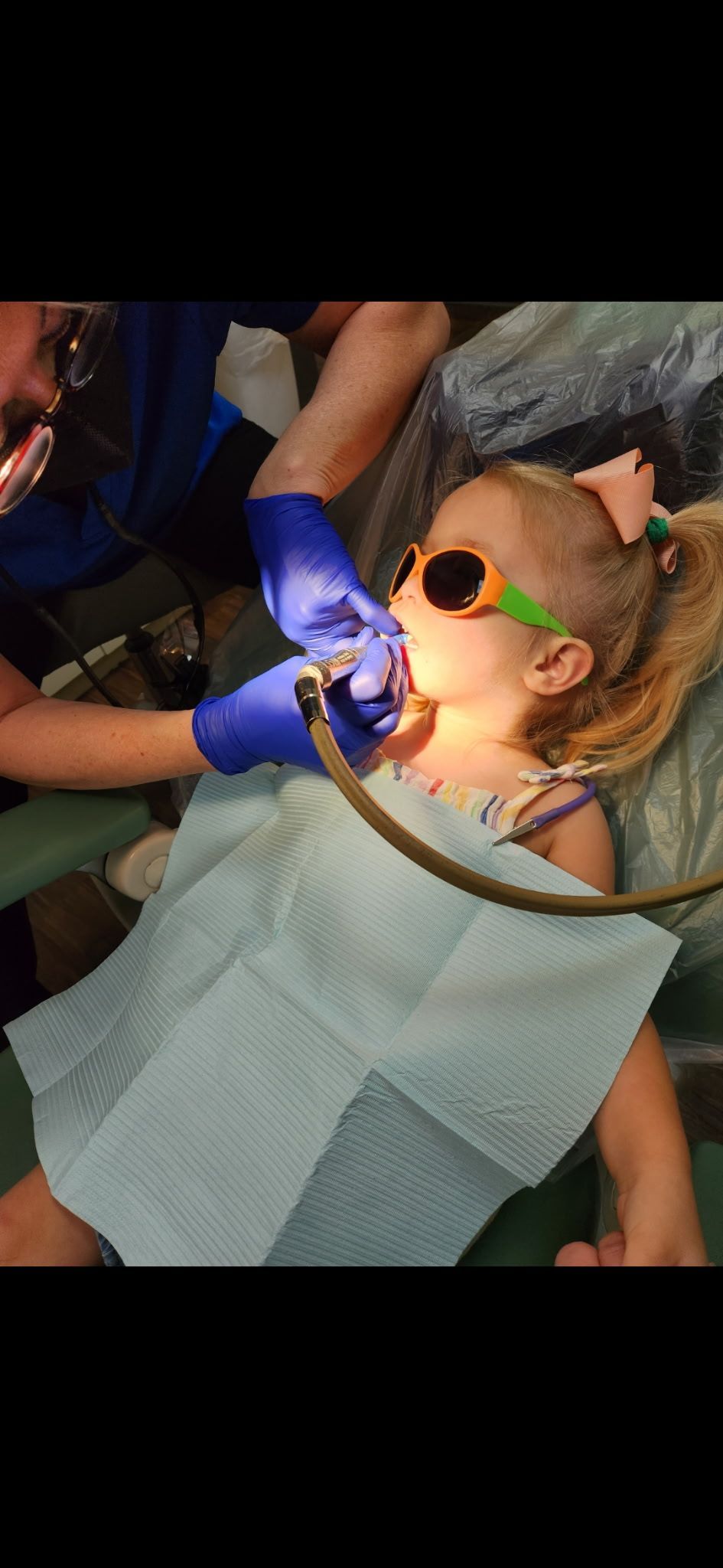 A little girl is sitting in a dental chair getting her teeth examined by a dentist.