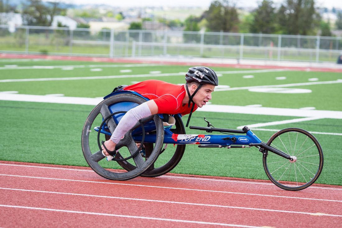 Chance Wells in a red top races a blue racing wheelchair on the track
