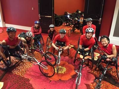 Racers in red shirts gather with their racing wheelchairs in a hotel lobby