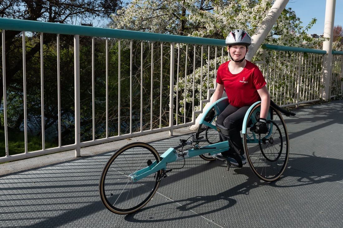Young racer in a red shirt sits in a teal racing chair on a footbridge