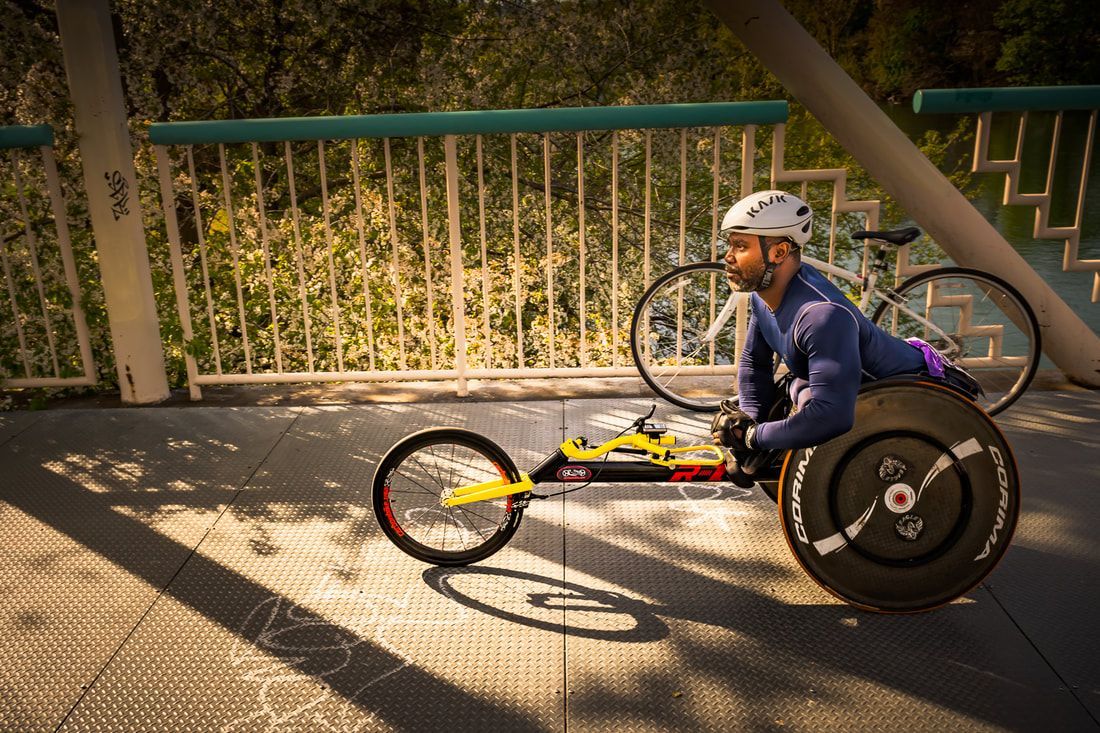Racer in a navy shirt and white helmet in a yellow racing chair on a bridge