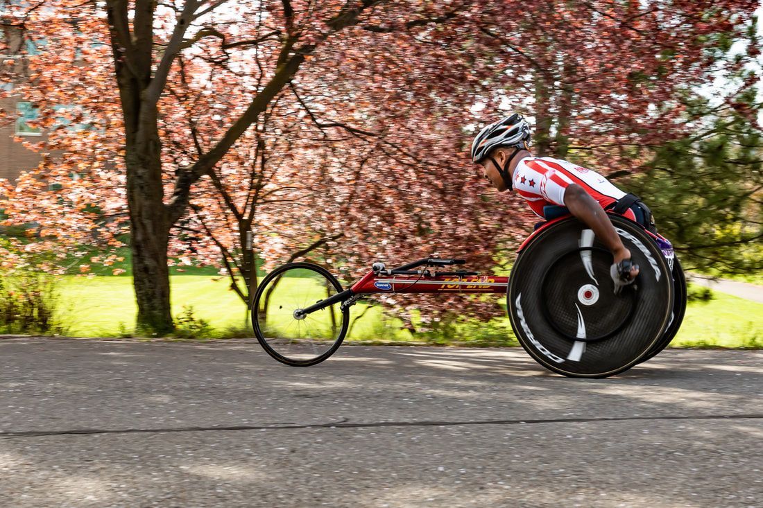 Racer in a stars-and-stripes jersey speeds past pink blossoming trees