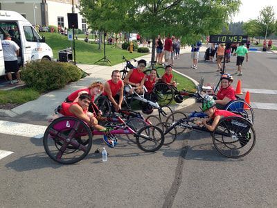 Racers in red gather in their racing wheelchairs near a race clock