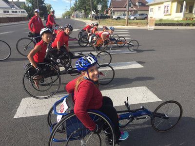 Racers in red shirts line up in racing wheelchairs at a crosswalk