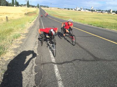Two racers in red approach the camera on a country road
