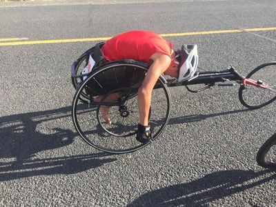 Racer in red rests, head down over the knees, in a racing wheelchair