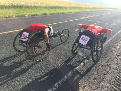 Racers 460 and 462 rest bent forward in their racing wheelchairs on the road