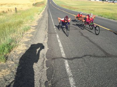 Three racers in red push up the road toward the photographer
