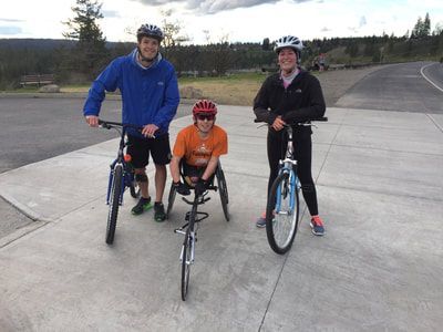 Young racer in an orange shirt poses between two cyclists on a path