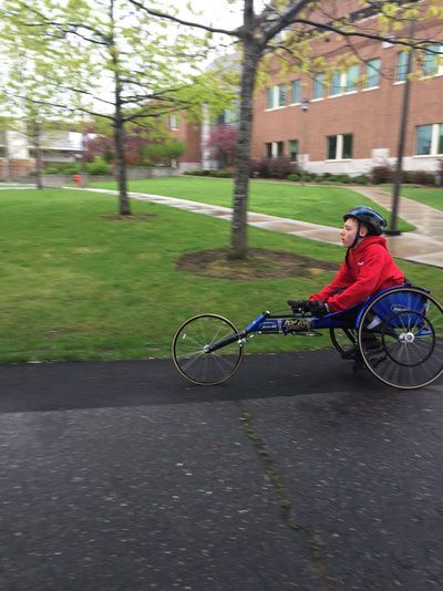 Racer in a red jacket pushes along a campus sidewalk