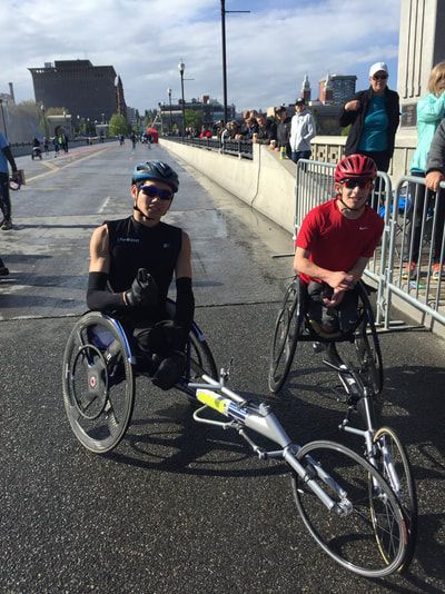 Two racers pose on a bridge as spectators gather behind barriers