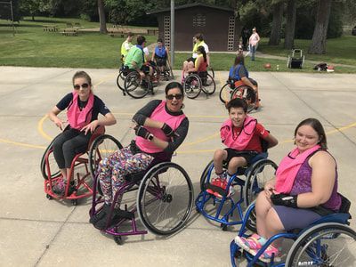 Four players in pink pinnies sit in sport wheelchairs on an outdoor court