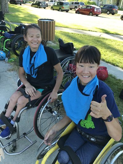 Two smiling athletes with blue towels at their necks, one gives a thumbs up