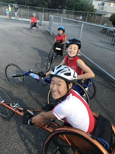 Young racers in helmets line up in racing wheelchairs on pavement