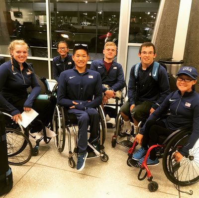 Athletes in Team USA jackets pose together indoors, most in wheelchairs