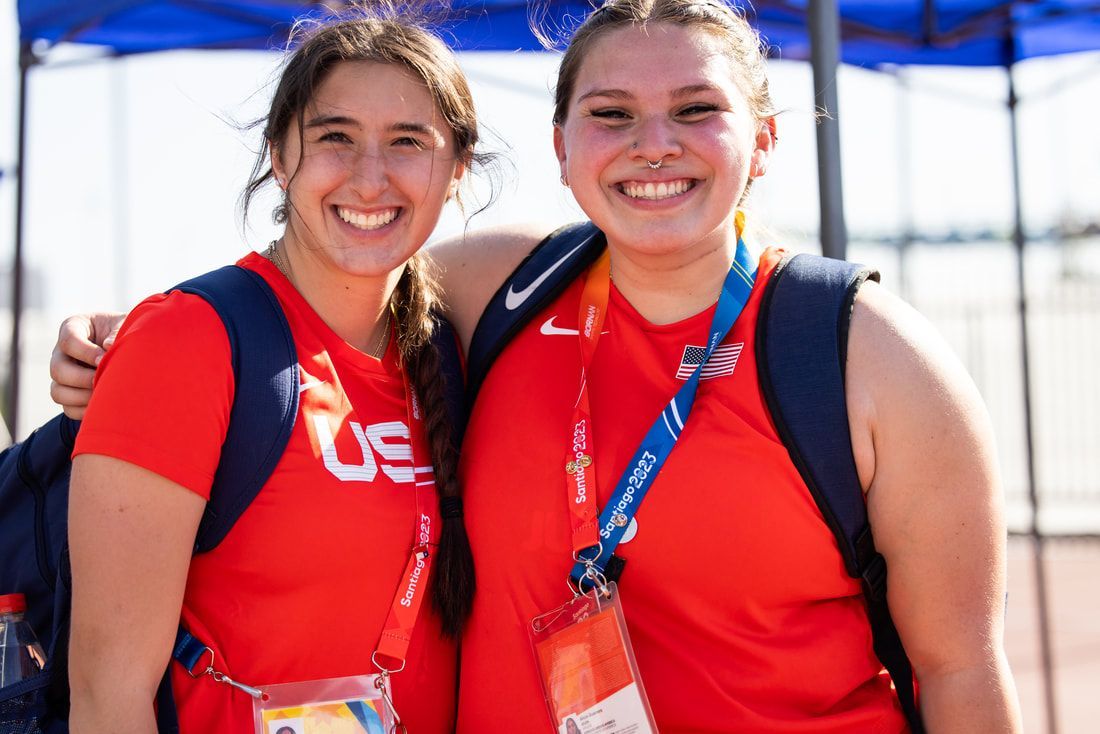 Two smiling Team USA athletes in red shirts pose arm in arm