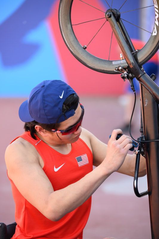 Phillip Croft in a blue cap adjusts a wheel on his racing chair