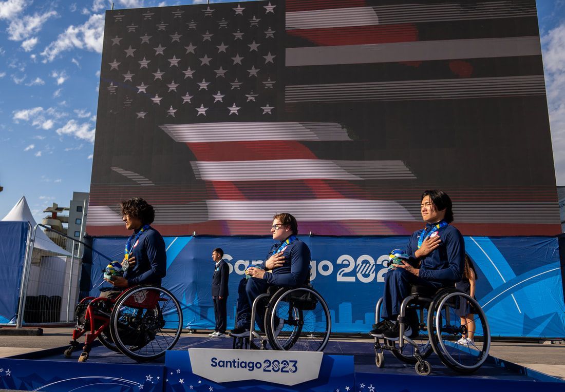 Three Team USA wheelchair racers on the podium, hands on hearts