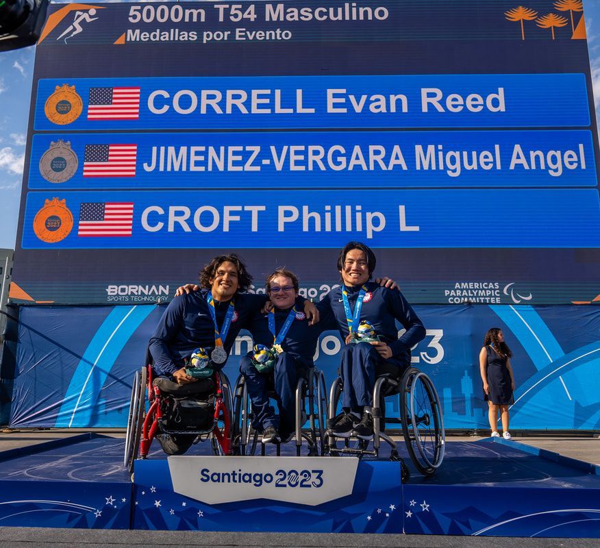 Three Team USA racers on the men's T54 5000m podium, results board above
