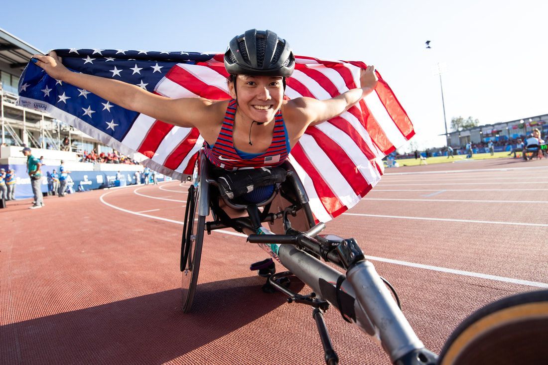Hannah Dederick on the track with an American flag held wide behind her