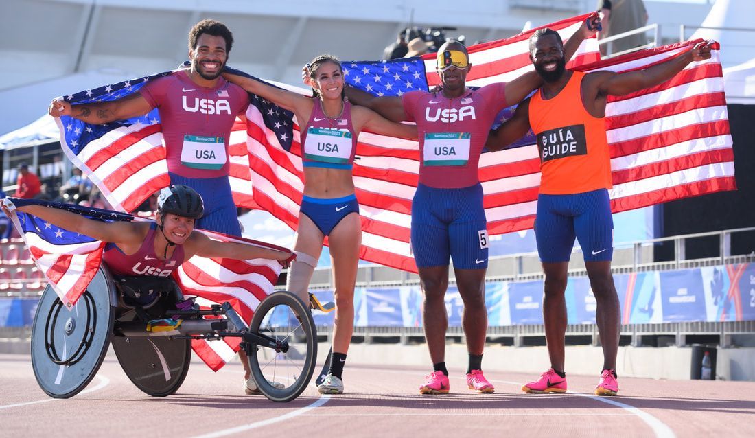 Four Team USA athletes and a guide runner celebrate with American flags