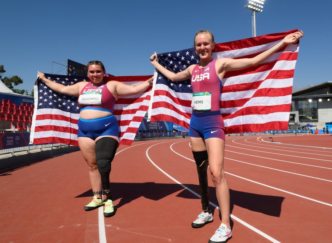Two Team USA athletes with prosthetic legs raise American flags on the track