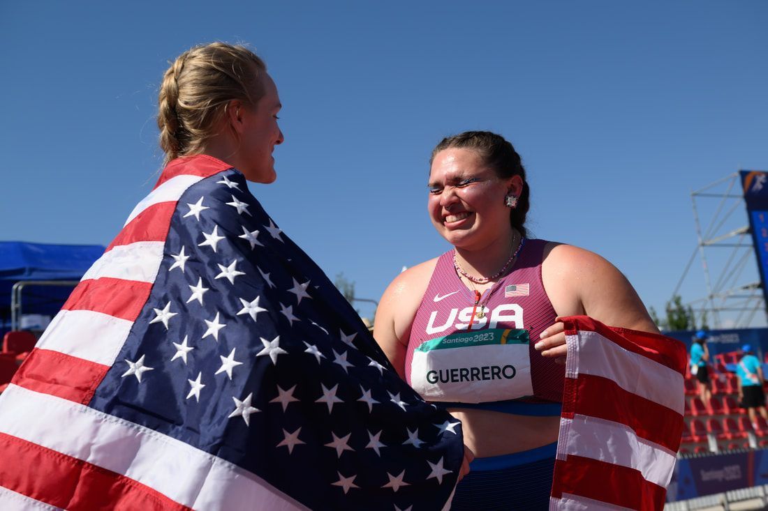 Two Team USA throwers celebrate together, one wrapped in an American flag