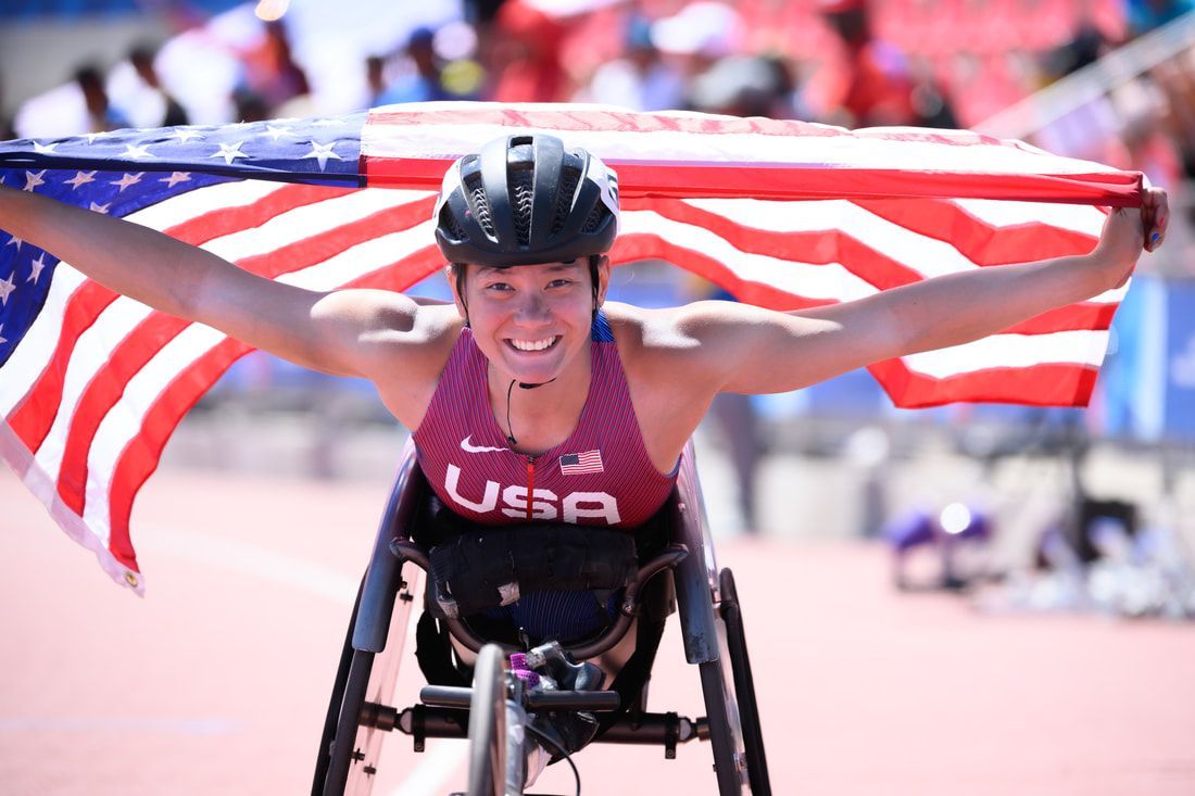 Hannah Dederick smiles in her racing chair, American flag spread behind her