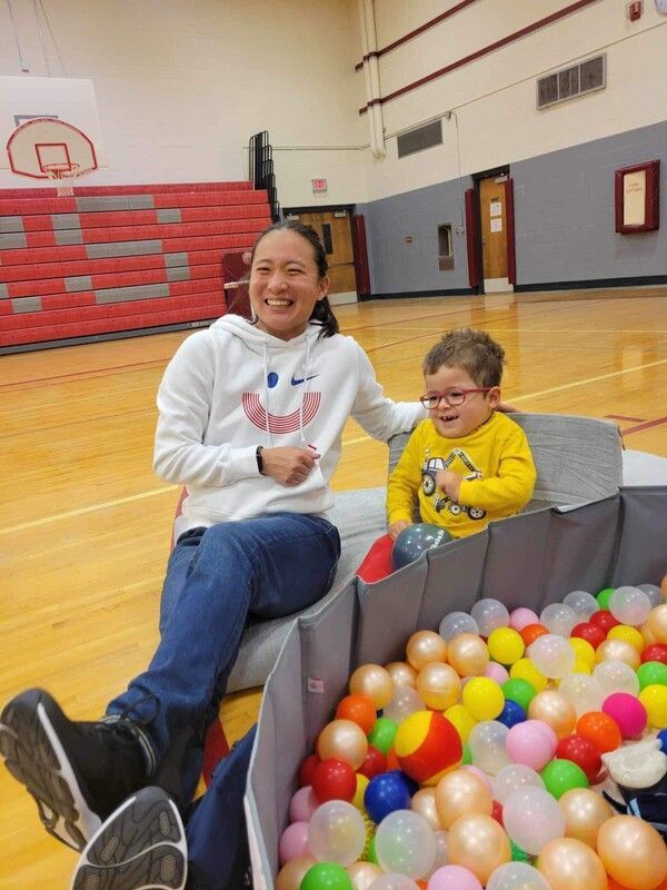 Coach and a young child in yellow sit by a colorful ball pit in the gym