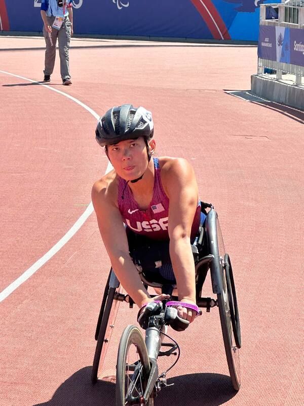 Wheelchair racer in a maroon USA top smiles on the track after a race