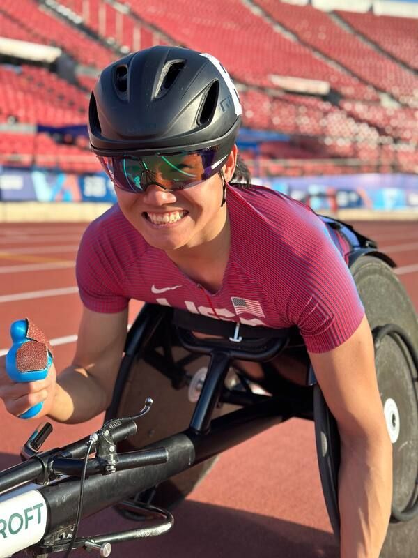 Smiling wheelchair racer in mirrored glasses gives a thumbs up