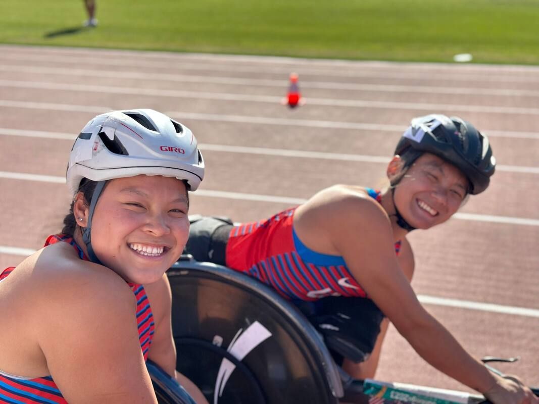 Two smiling wheelchair racers in Team USA tops on the track