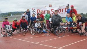 ParaSport track team with racing wheelchairs poses on a track by a banner