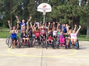 Wheelchair basketball players cheer with arms raised under a Hoopfest hoop