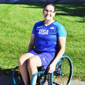 Rachael Morrison in a Team USA shirt sits in her wheelchair on the grass
