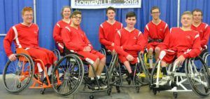 Team in red warm-ups poses in wheelchairs under a Louisville 2016 banner