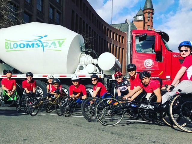 Racers in racing wheelchairs and handcycles line up by a Bloomsday truck