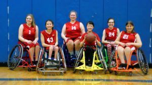 2016 women's team in red jerseys sits in a row with a basketball