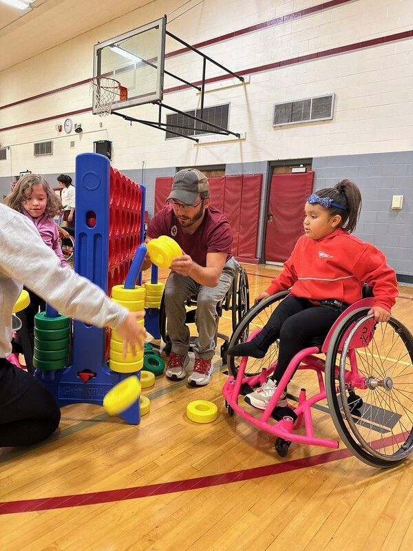 Kids in wheelchairs play a giant Connect Four game with adults in the gym