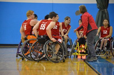 Coach in a red jacket talks to players in red jerseys during a huddle